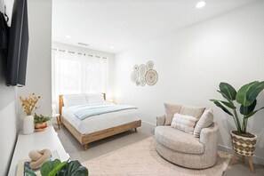Ein Schlafzimmer mit einem Bett, einem Sofa, einer Zimmerpflanze und einer Wanddekoration.