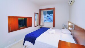 Ett hotellrum med en säng, ett fönster med utsikt, en väggmonterad luftkonditioneringsanläggning och ett nattduksbord med en lampa.