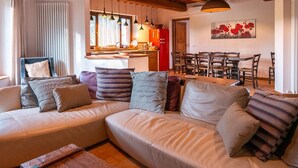 Un salón acogedor con un sofá modular, vigas de madera, iluminación colgante y vistas al área de la cocina.