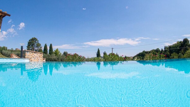 Una piscina azul cristalina con una estructura de piedra a un lado y vistas al cielo y árboles al fondo.