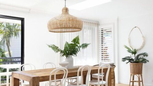 A dining area with a wooden table and chairs, a hanging light fixture, and potted plants.