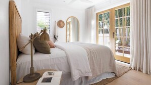 A bedroom with a bed, a bedside lamp, a mirror, and a window with curtains.