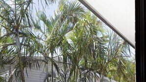 A balcony with a white table and bench, surrounded by palm trees.