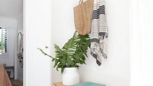 A wooden bench with a woven basket underneath, a potted plant, a book titled "SURF TRIBE", and a hanging bag.
