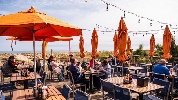 Zona pranzo all'aperto con tavoli e ombrelloni arancioni, con vista sulla spiaggia.