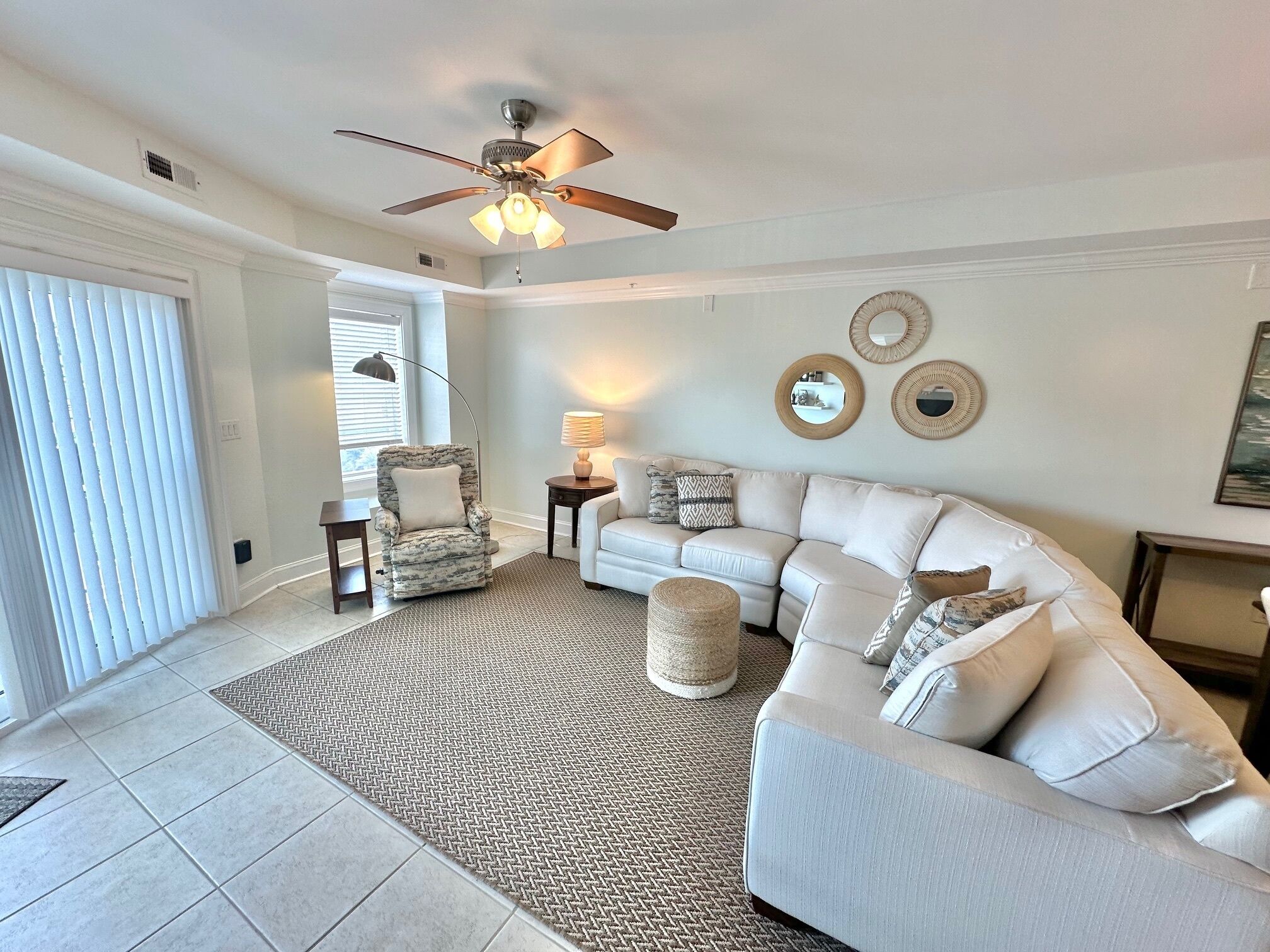 A living room with a sectional sofa, a ceiling fan, and a patterned rug.