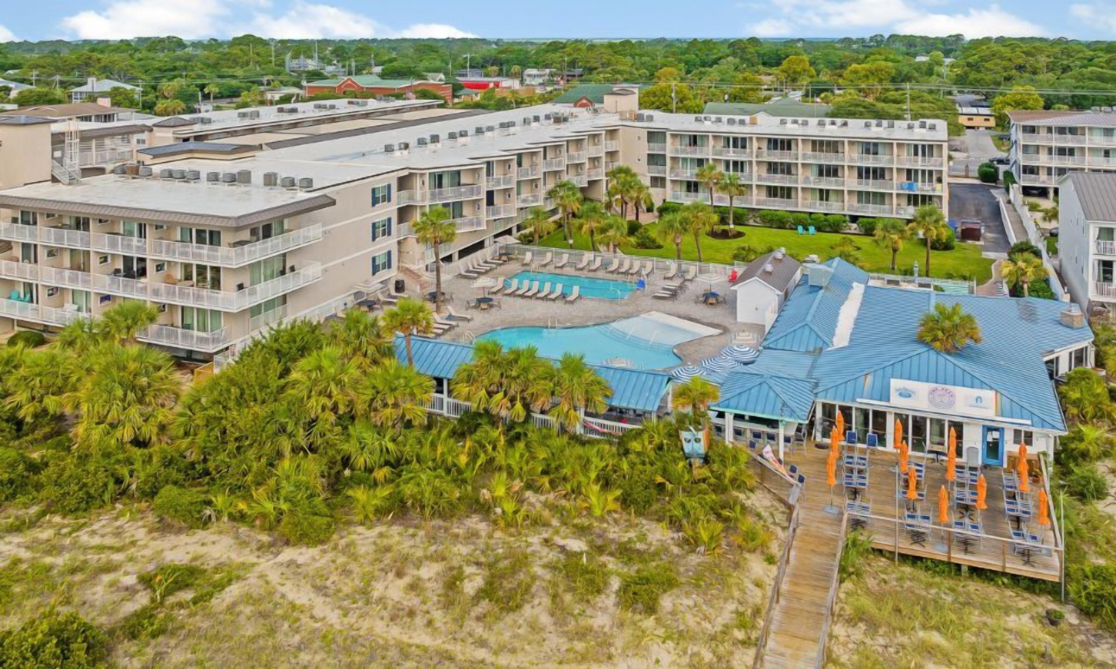 A resort with multiple buildings, a swimming pool, and a beach area with lounge chairs.