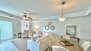 A modern living room with a white sofa, a wooden dining table, and a ceiling fan. - Summer & July 4th Savings at Beachside Colony Tybee's ONLY Oceanfront Resort 3/2 (Tybee Island)