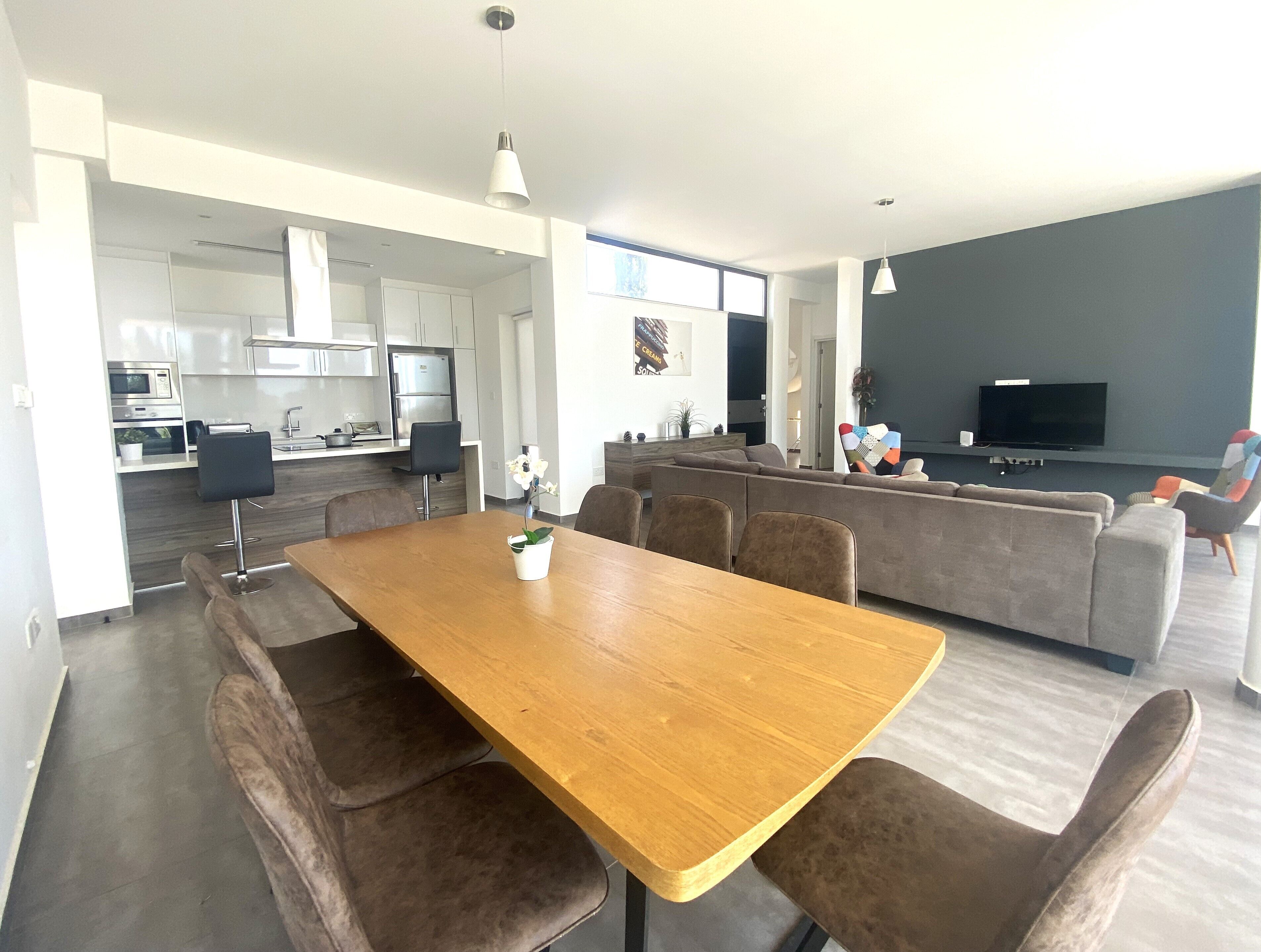 Un espacio de estar moderno con comedor, cocina y zona de estar con televisor.