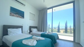 A hotel room with two beds, a large window with a city view, and a painting on the wall.