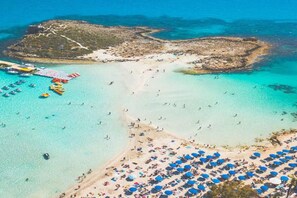 An aerial view of a beach with clear turquoise waters, a sandy shore, and numerous umbrellas.