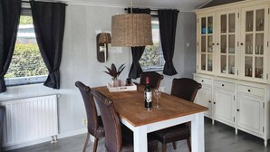Spisestue med et træbord, fire stole, en hængende lampe og et skab med glasdøre.
