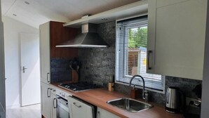 Et moderne køkken med hvide skabe, en stålvask, indbygget ovn og et vindue med persienner.