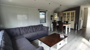 En moderne stue med en hjørnesofa, et træsofabord og et spiseområde med et hvidt bord og mørke stole.