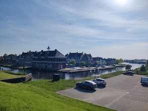 A canal-side building with a waterway, parked cars, and a grassy area. - Paloma Chalet with Sauna - Relaxing Nature Escape by Lauwersmeer Park (Anjum)