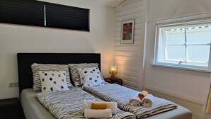 Un lit double avec une literie à rayures, une lampe de chevet et une fenêtre avec des stores.