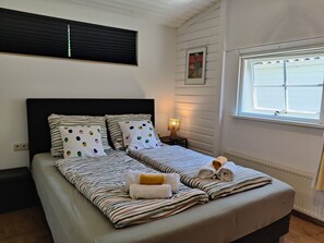 Ein Doppelbett mit gestreifter Bettwäsche, eine Nachttischlampe und ein Fenster mit Jalousien.