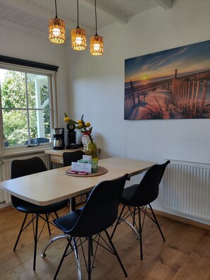 A dining area with a table, chairs, a painting, and hanging lights. - Paloma Chalet with Sauna - Relaxing Nature Escape by Lauwersmeer Park (Anjum)