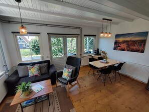 Ein Zimmer mit einer Couch, einem Esstisch, Stühlen, einer Kaffeemaschine und einem Bild an der Wand.