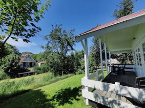 A covered outdoor area with a wooden deck, a white railing, and a view of a house in the background.