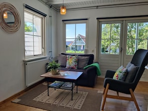 A cozy living room with a sofa, a chair, a coffee table, and a window overlooking a house. - Paloma Chalet with Sauna - Relaxing Nature Escape by Lauwersmeer Park (Anjum)