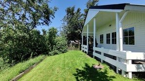 A white building with a porch, surrounded by lush greenery and trees. - Paloma Chalet with Sauna - Relaxing Nature Escape by Lauwersmeer Park (Anjum)