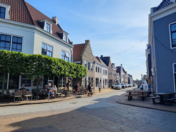 A cobblestone street lined with buildings, outdoor seating, and a dog walking. - Paloma Chalet with Sauna - Relaxing Nature Escape by Lauwersmeer Park (Anjum)