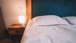 Een keurig opgemaakt bed met witte lakens en kussens, een nachtkastje met een lamp, en een houten hoofdbord.