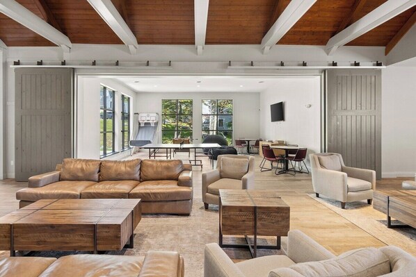 A spacious living room with leather sofas, wooden coffee tables, and a large dining area with a view of the outdoors. - The Alpine Escape | Slope-Side Condo at Mount Snow (Dover)