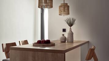 Een moderne eetruimte met een houten tafel, twee hangende rieten lampen en een vaas met een plant.