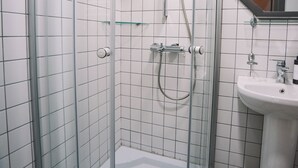 A glass-enclosed shower with a white tiled wall, a glass shelf, and a white sink with a mirror above it. - Rooftop Grey Apartment at Rustaveli Avenue (T'bilisi)