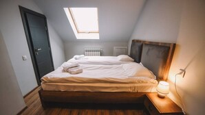 A bedroom with a skylight, a bed with white linens, a bedside table with a lamp, and a radiator. - Rooftop Grey Apartment at Rustaveli Avenue (T'bilisi)