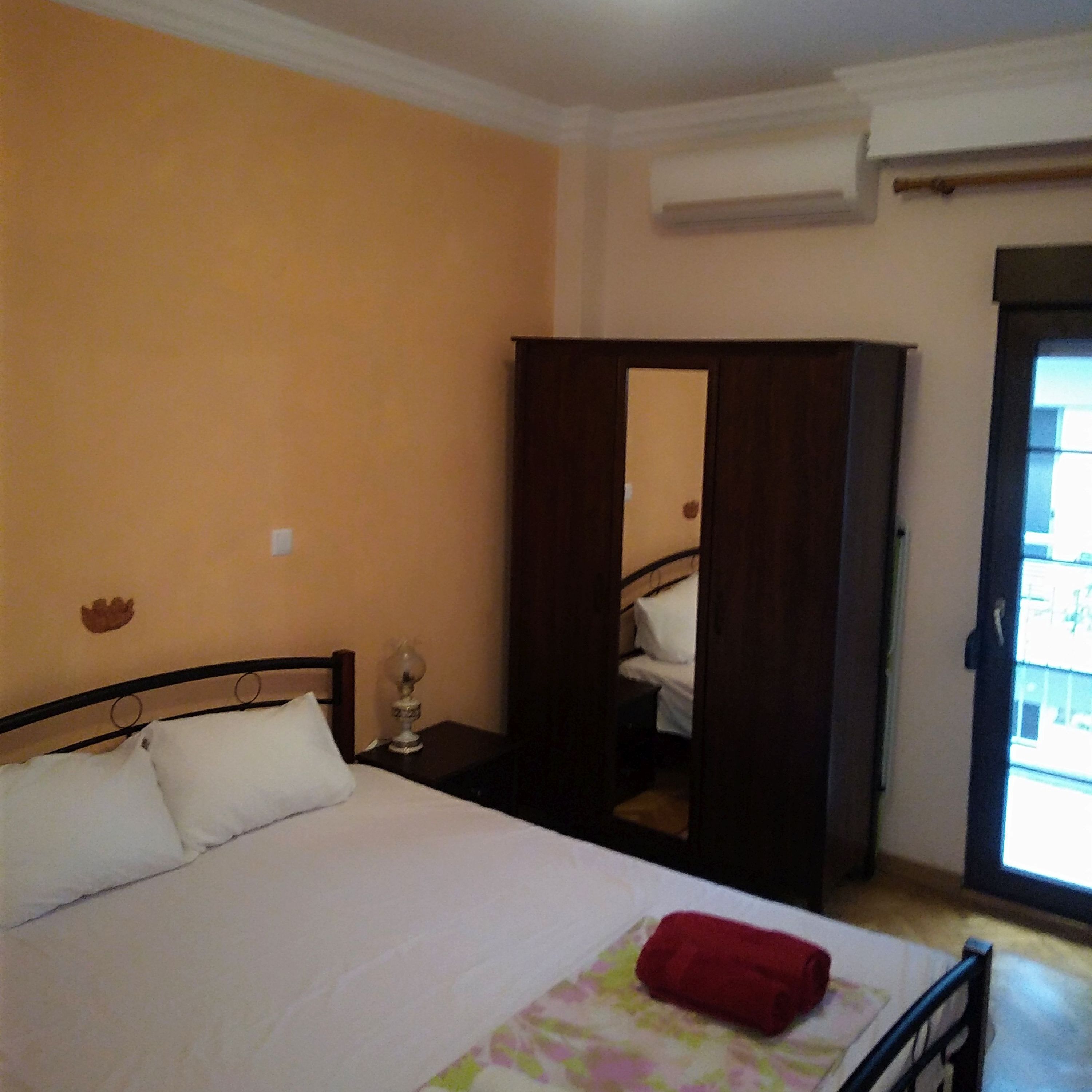 Une chambre à coucher comprenant un lit, une table de chevet, un miroir et une porte donnant sur une autre pièce.