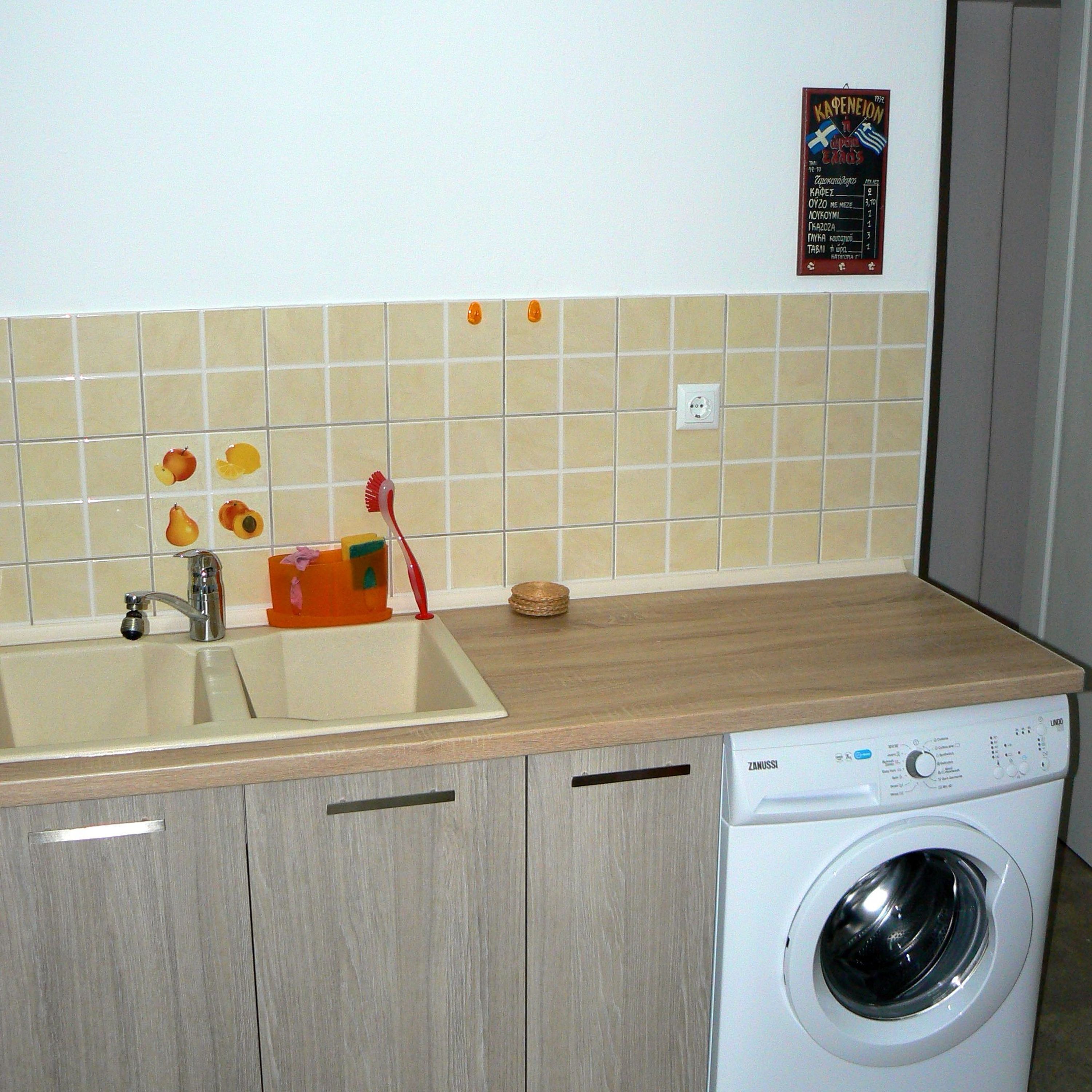 Una cocina con un lavamanos, lavadora y salpicadero de azulejos.