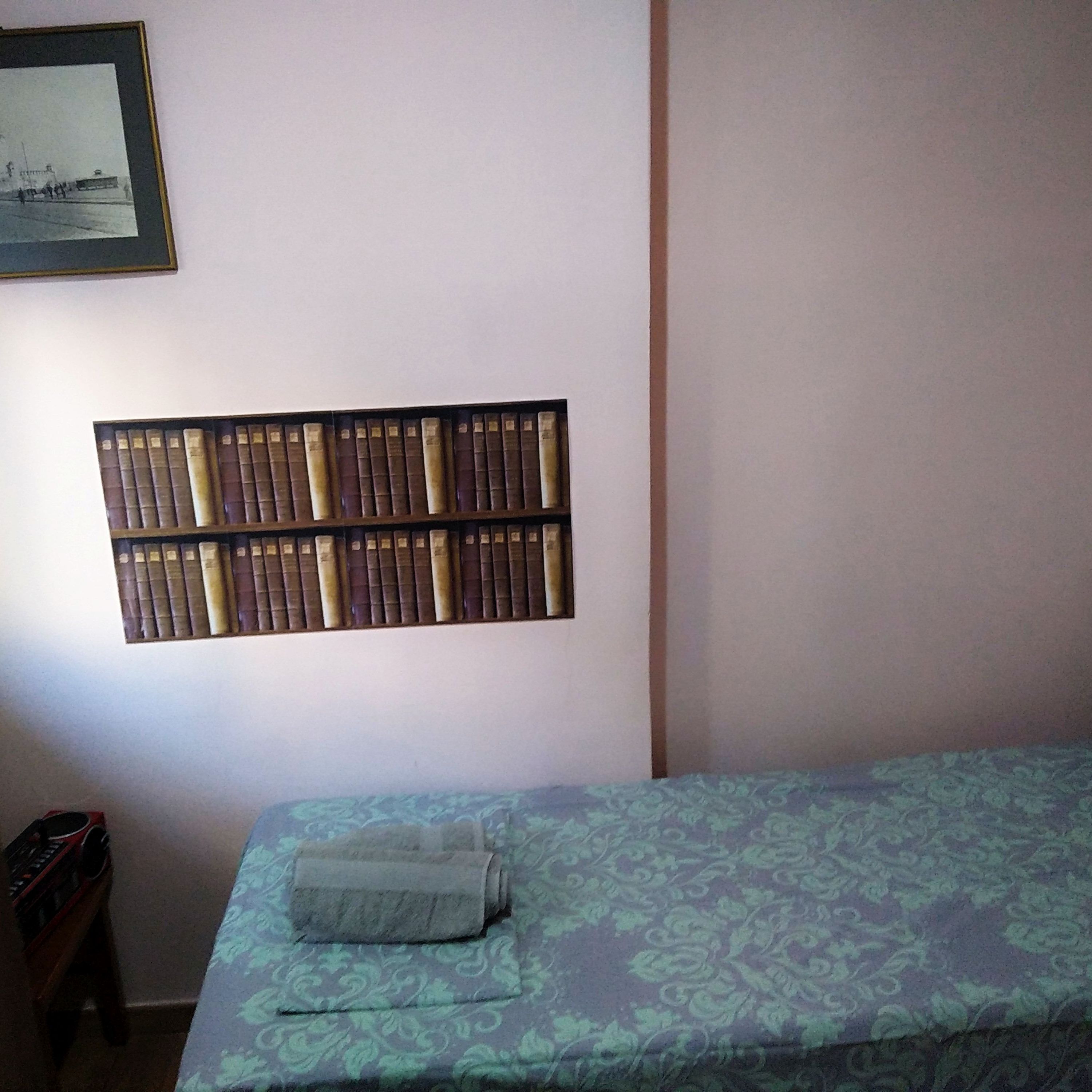 A room with a bed, a bookshelf, and a framed picture on the wall.