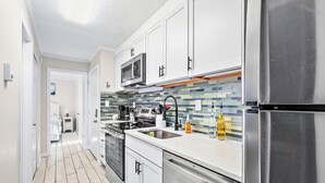 A modern kitchen with white cabinets, a stainless steel refrigerator, a microwave, and a tiled backsplash. - Ocean and Bay view luxury condo with balcony  (Ocean City)