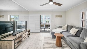 A modern living room with a flat-screen TV, wooden entertainment unit, grey sofa, and a ceiling fan. - Ocean and Bay view luxury condo with balcony  (Ocean City)