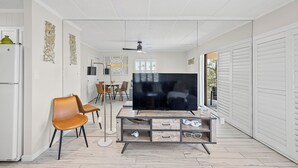 A modern living room with a flat-screen TV, a wooden entertainment unit, and a dining area with chairs and a table. - Ocean and Bay view luxury condo with balcony  (Ocean City)