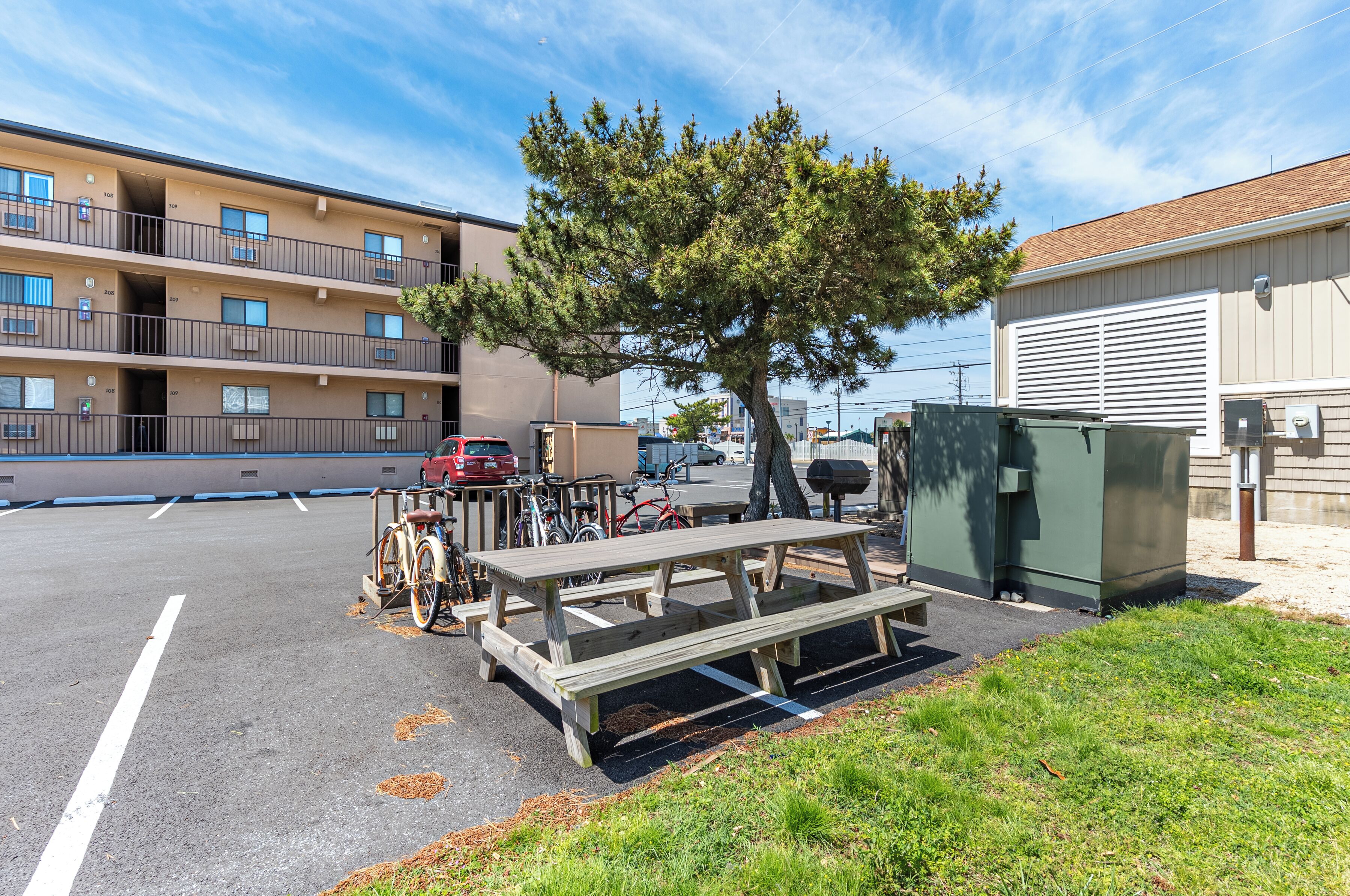 Un espace de stationnement extérieur équipé de tables de pique-nique, de vélos et d’un arbre.