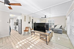 Uma sala de estar moderna com televisão, móvel para aparelhos eletrônicos de madeira e ventilador de teto.