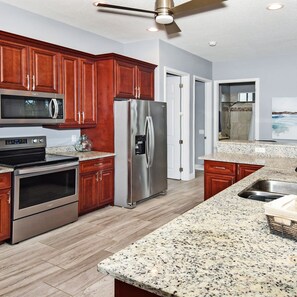 A modern kitchen with wooden cabinets, stainless steel appliances, granite countertops, and a ceiling fan. - Phoenix Quite Area Pool and Great Water few (Cape Coral)