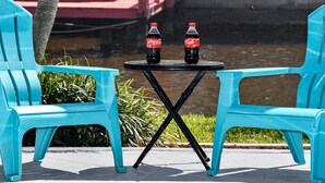 Kaksi turkoosinsinistä tuolia pienen mustan pöydän ympärillä, ja pöydällä on kaksi Coca-Cola-pulloa.