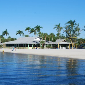 A beachside building with a flat roof, surrounded by palm trees and a sandy beach.