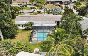 A residential area with a house featuring a screened-in pool area, surrounded by lush greenery and palm trees.
