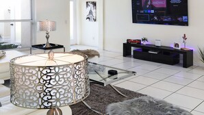 A modern living room with a white sofa, a decorative lamp, a glass coffee table, a television, and a ceiling fan. - Su Casa - XXL Pool Area Pool Spa 3 Bedroom 2 Bath (Cape Coral)