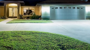 A residential house with a garage, a well-lit entrance, and a lawn. - Su Casa - XXL Pool Area Pool Spa 3 Bedroom 2 Bath (Cape Coral)
