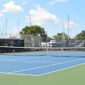 A tennis court with a net, surrounded by a chain-link fence, palm trees, and a clear sky. - Boaters Dream S Terr Pool Yacht Club Boating (Cape Coral)