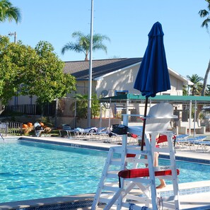 A swimming pool with lounge chairs and umbrellas, a lifeguard chair, and a building in the background. - Boaters Dream S Terr Pool Yacht Club Boating (Cape Coral)