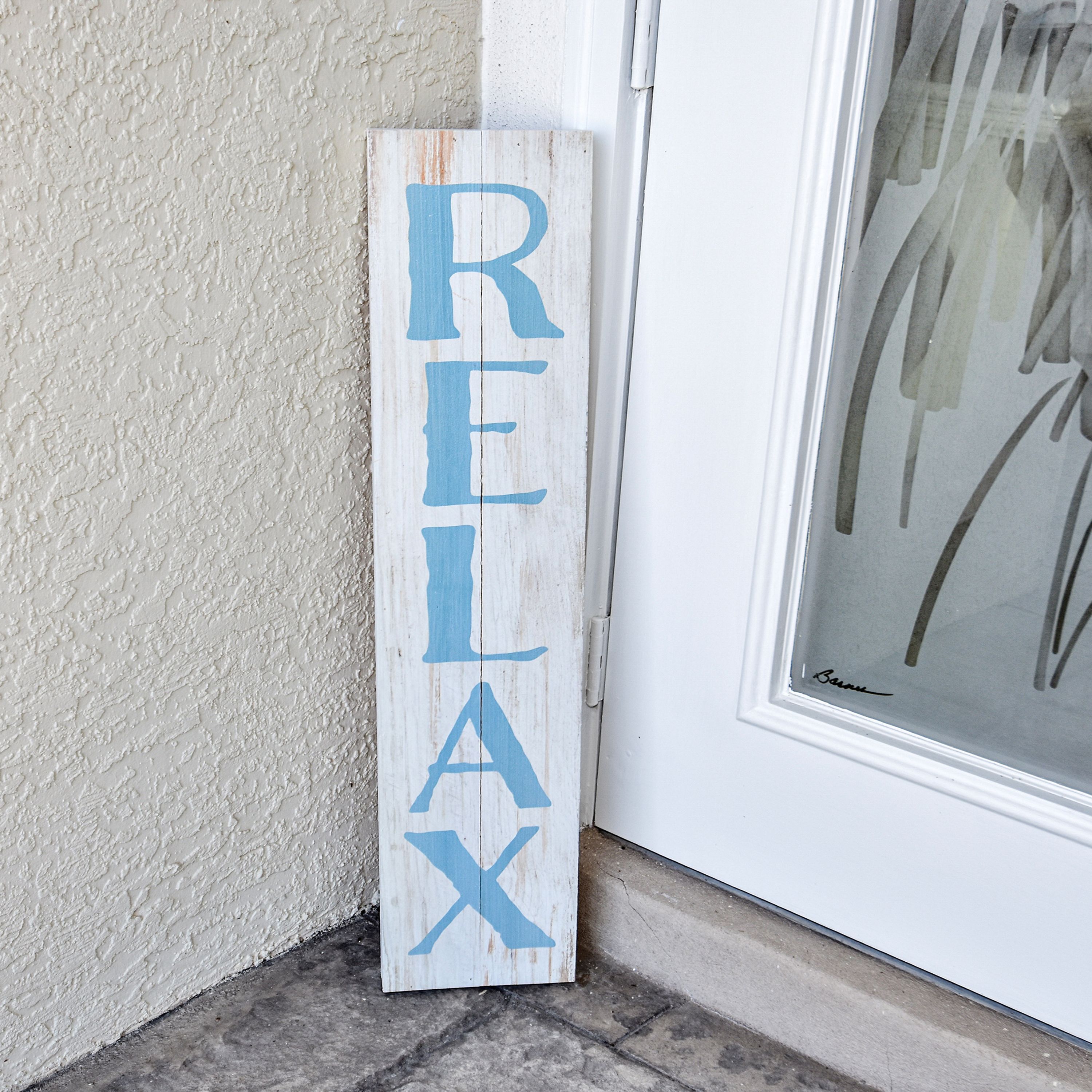 Siniseksi maalattu puinen kyltti, jossa on sana ”RELAX”, nojaa valkoista ovea vasten.