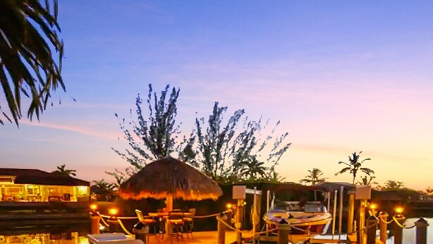 A poolside area with a thatched-roof structure, lounge chairs, and a dining table.